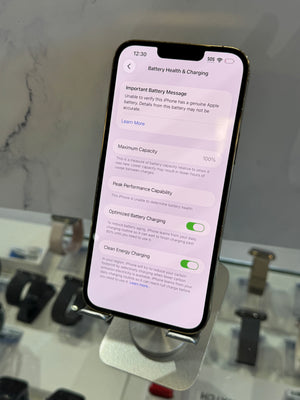 A smartphone displaying the Battery Health & Charging settings screen, held upright in a retail display stand with watch bands blurred in the background.