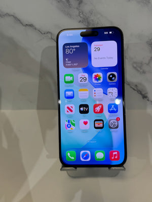A black Apple iPhone with a lit home screen, resting on a small metal display stand against a light marble-patterned background.