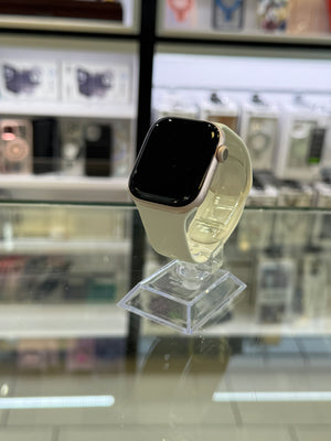A smartwatch with a light beige band and a gold-toned case, displayed on a clear stand inside a retail store.