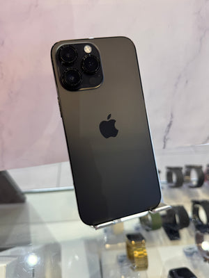 A black Apple iPhone 12 Pro shown from the back, resting on a display stand in a retail setting with a marble-patterned wall in the background.