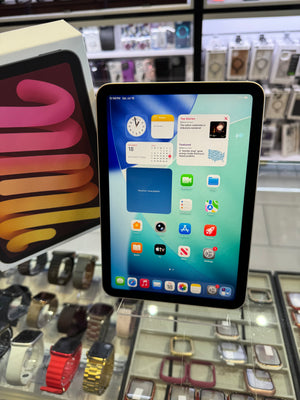 A black Apple iPad displaying its home screen, standing on a glass display counter in a retail store with watches and accessories in the background.