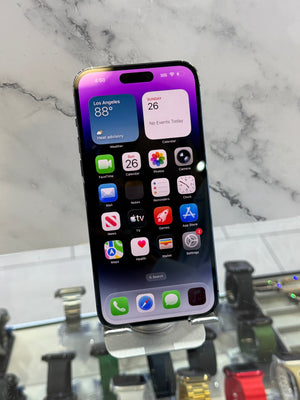 A black iPhone with its screen on, resting on a white and gray marble surface with a display stand visible in the background.