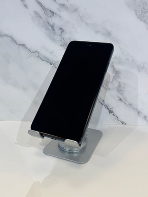 A black smartphone displayed upright on a silver metal stand against a white marble-patterned background.