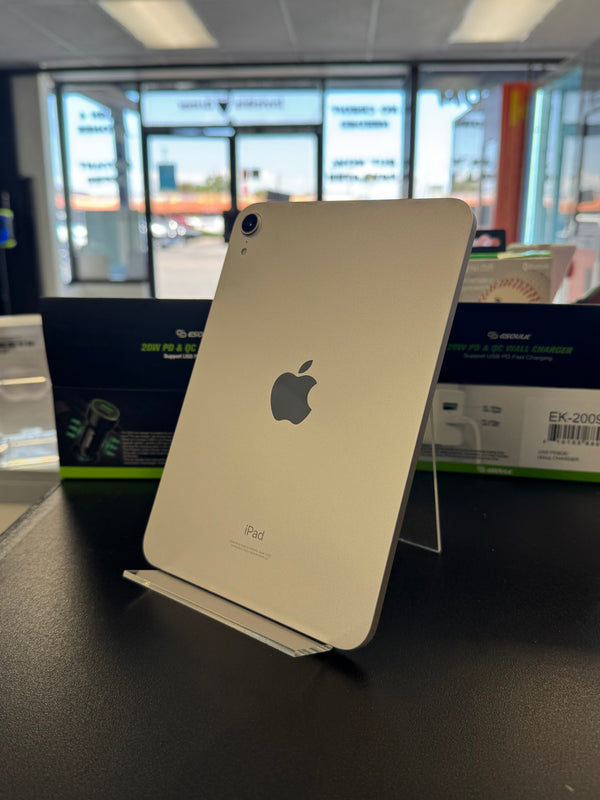 A gold Apple iPad standing upright on a clear display stand on a dark counter, with store windows and products blurred in the background.