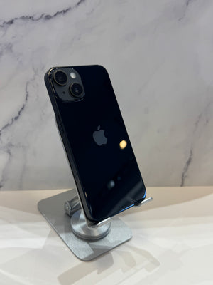 A black Apple iPhone 13 back is displayed on a silver metal stand against a light gray marble-patterned background.
