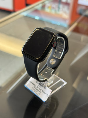 A black smartwatch with a black band, shown resting on a reflective glass display counter with a price tag attached.