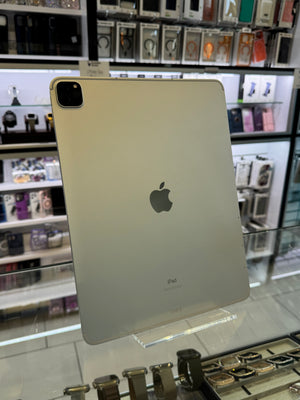 A silver Apple iPad shown from the back, resting on a glass display counter inside a retail store with shelves of accessories visible in the background.