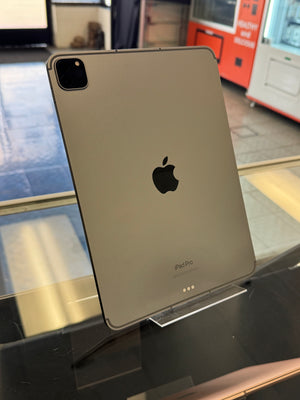 A silver Apple iPad shown from the back, resting on a reflective glass surface with a store or office background visible.