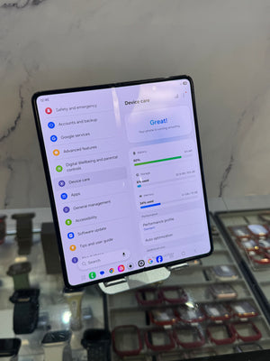 A Samsung Galaxy Z Flip 3 foldable smartphone displaying the Android device settings menu, standing on a small display stand in a retail environment.