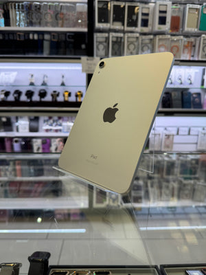A silver Apple iPad shown from the back, displayed on a clear stand inside a retail store with shelves of accessories in the background.