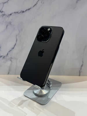A black Apple iPhone 12 Pro shown from the back, resting on a silver metal stand against a white marble-patterned background.