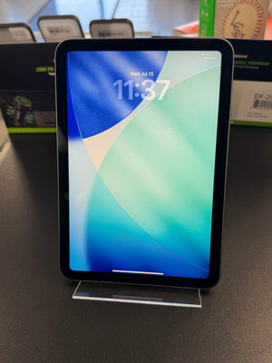 A black tablet with a colorful blue and green lock screen wallpaper, displayed upright on a clear acrylic stand on a dark tabletop.