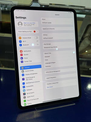 A tablet device shown from above, displaying the iPad Settings interface on its screen against a blue and metallic background.