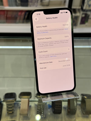 A black smartphone displaying battery health information on its screen, photographed inside a retail display with watches and glass cases visible in the background.