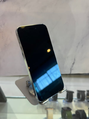 A silver smartphone with a black screen, displayed on a small stand in a retail setting with a marble-patterned background.