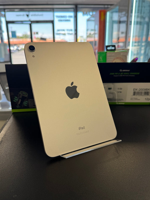 An Apple iPad shown from the back in a light gold finish, resting on a dark surface with its retail box partially visible behind it.