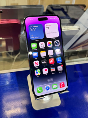A black iPhone with a purple and pink gradient lock screen displaying the home interface, resting on a silver metal stand on a blue counter in a retail setting.