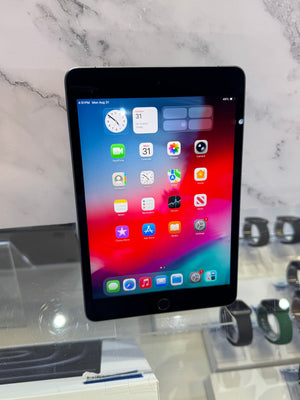 A black Apple iPad tablet with its screen turned on, displaying the home screen, set against a marble-patterned background with watch displays on a counter in the foreground.