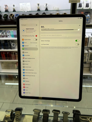 An iPad displaying the Apple Settings app, standing on a clear display stand inside a retail store with watches visible in the background.