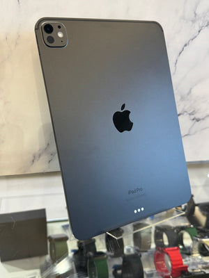 A dark gray Apple iPad Pro shown from the back, standing on a display stand in front of a marble-patterned wall.