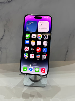 A black iPhone with a purple and pink dynamic wallpaper displayed on a silver metal stand, set against a gray marble-patterned background.