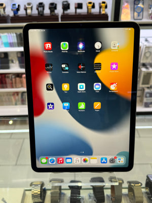 A black tablet with a lit home screen, photographed in a retail display area with shelves and other devices blurred in the background.
