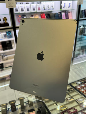 A silver Apple iPad Air standing upright showing the back with the Apple logo, inside a store setting