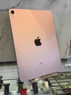 A rose gold Apple iPad shown from the back, resting on a glass display stand in front of a white marble-patterned background.