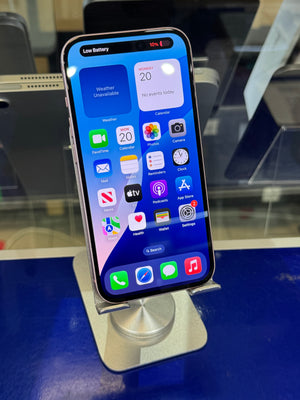 A black Apple iPhone with a lit screen displaying various colorful app icons, resting on a silver metal stand on a blue surface.