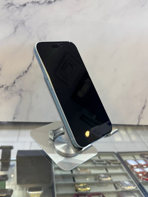 A silver smartphone with a black screen stands on a metallic display stand in front of a white marble-patterned wall.