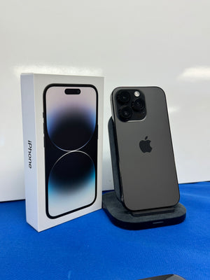 A dark gray Apple iPhone 14 Pro shown from the back next to its original white retail box on a blue surface against a white wall.