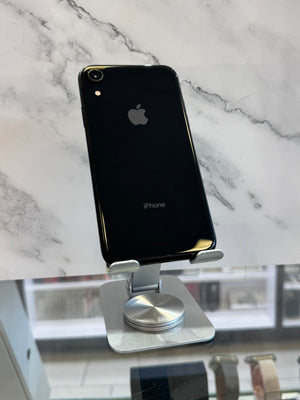 A black Apple iPhone XR standing upright on a silver metal display stand, photographed against a white marble-patterned background.