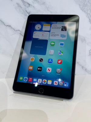 An iPad Pro with a black bezel and home button, displaying its home screen, resting on a clear acrylic stand against a white marble background.