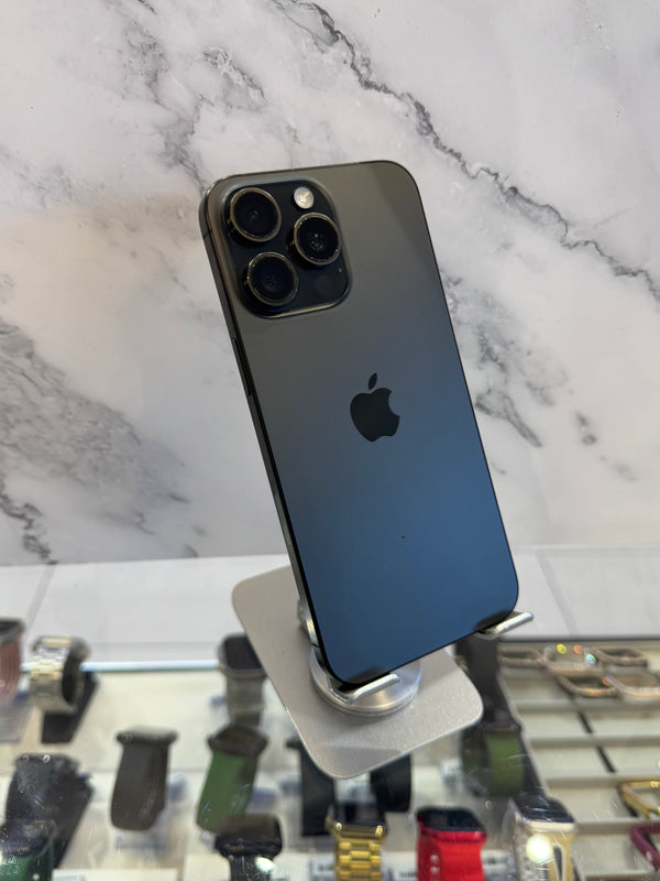 A dark gray Apple iPhone 12 Pro shown from the back, resting on a white and gray marble-patterned surface with a watch display case visible in the background.