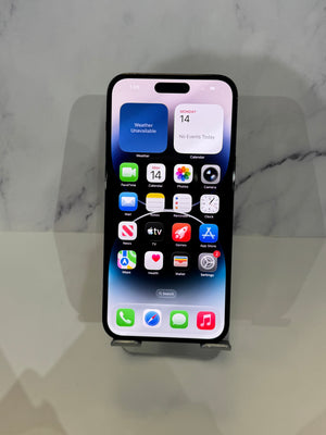A black Apple iPhone with a lit home screen, displayed upright on a small stand against a light gray marble-patterned background.