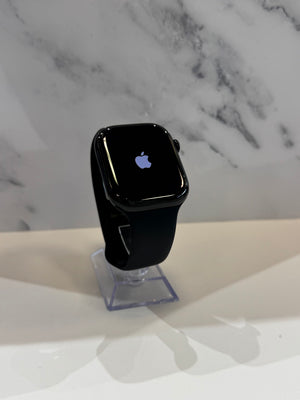 Black Apple Watch with a black band displayed on a clear stand against a white marble-patterned background.