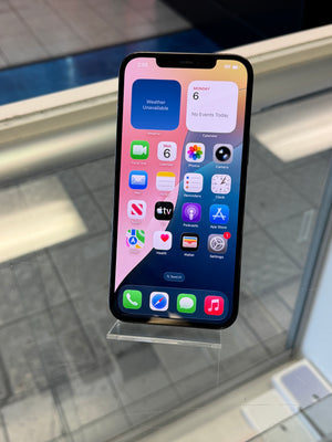 A black iPhone with the home screen visible, photographed from above on a glass display stand in a retail or showroom setting.
