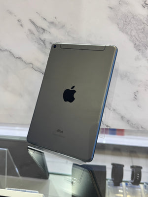 An Apple iPad with a dark gray metallic back and a blue side edge, standing on a glass display stand against a white marble background.