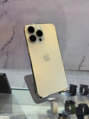 A gold Apple iPhone Pro showing its back panel with three rear cameras, displayed on a stand in a retail setting.