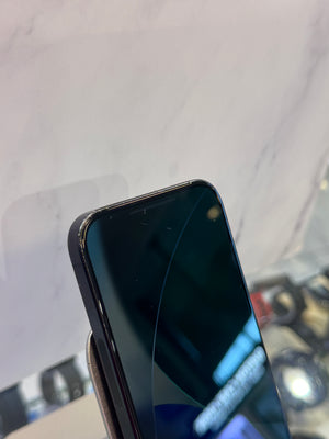 A close-up of a black smartphone with a front-facing camera cutout, resting on a display stand against a light gray marble-patterned background.