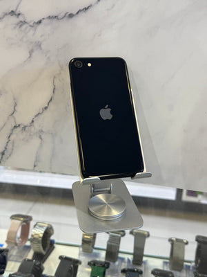 A black Apple iPhone with a silver metallic bumper is displayed on a silver metal stand on a white marble surface.