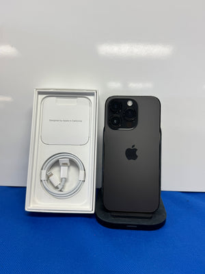 A black Apple iPhone 12 Pro shown next to its original white packaging box containing a white charging cable, set against a white background with a blue surface below.