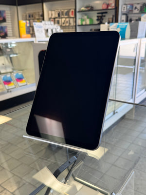 A black tablet device with a blank screen, displayed on a clear acrylic stand inside a retail store.