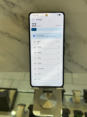 A black smartphone displaying the iOS storage settings screen, resting on a metallic display stand in a retail setting with a marble-patterned background.