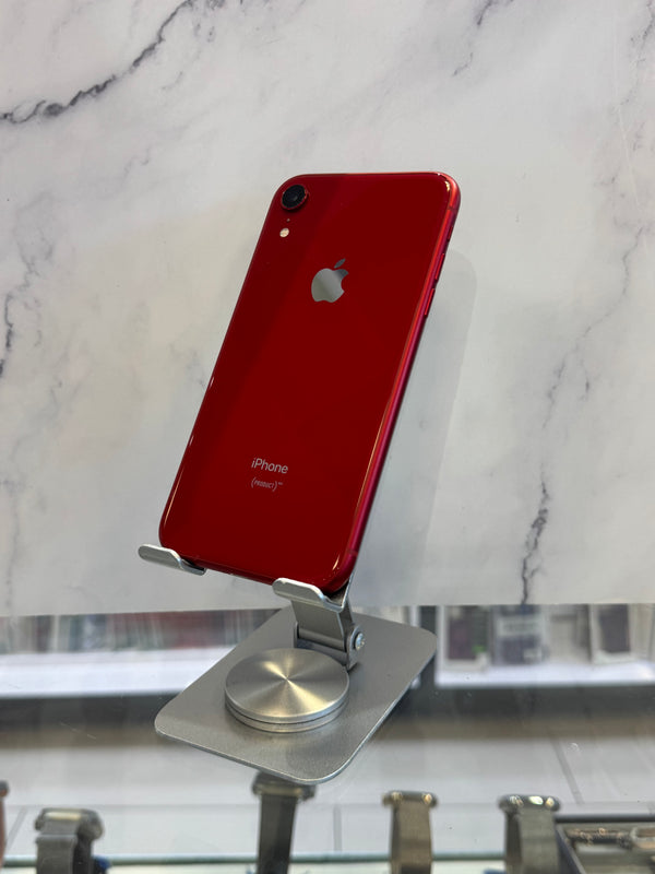 A red Apple iPhone XR displayed upright on a silver metal stand, showing the back of the phone against a white marble-patterned background.