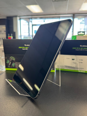 A black smartphone displayed upright on a clear acrylic stand on a dark tabletop, with retail packaging boxes visible in the blurred background.