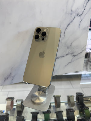 A gold-colored Apple iPhone Pro displayed on a silver metal stand, set against a white marble-patterned background with watch displays visible in the foreground.