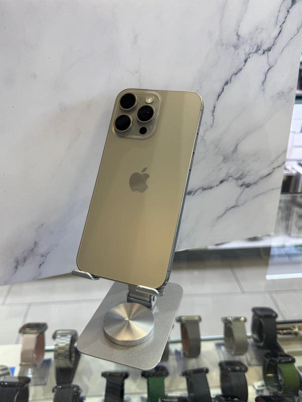 A gold-colored Apple iPhone Pro displayed on a silver metal stand, set against a white marble-patterned background with watch displays visible in the foreground.
