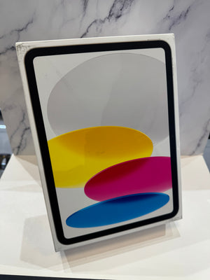 A white Apple iPad box standing upright on a white surface, with a marble-patterned background. The front of the box displays the Apple logo and abstract yellow, magenta, and blue shapes.