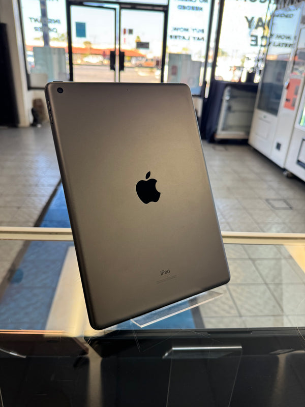 An Apple iPad with a dark gray metallic finish, standing upright on a clear display stand inside a retail store.